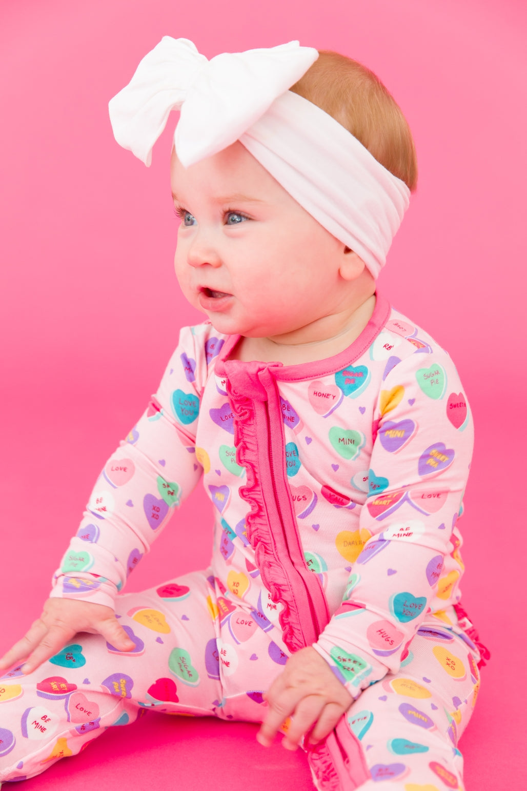 Model Wearing Rufflebutts + Ruggedbutts Baby Girls Be My Valentine Bamboo Viscose Footed Ruffle One Piece Pajama